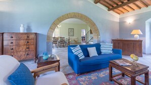 A living room with a blue sofa, wooden furniture, and a large archway leading to another room. - House / Villa - Magliano in toscana (Magliano in Toscana)