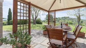 An outdoor patio with a wooden table and chairs, a pergola with a canopy, and a view of a green landscape. - House / Villa - Magliano in toscana (Magliano in Toscana)