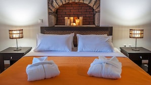 Een hotelkamer met een haard van baksteen, twee witte kussens, een oranje sprei en twee bedlampjes.