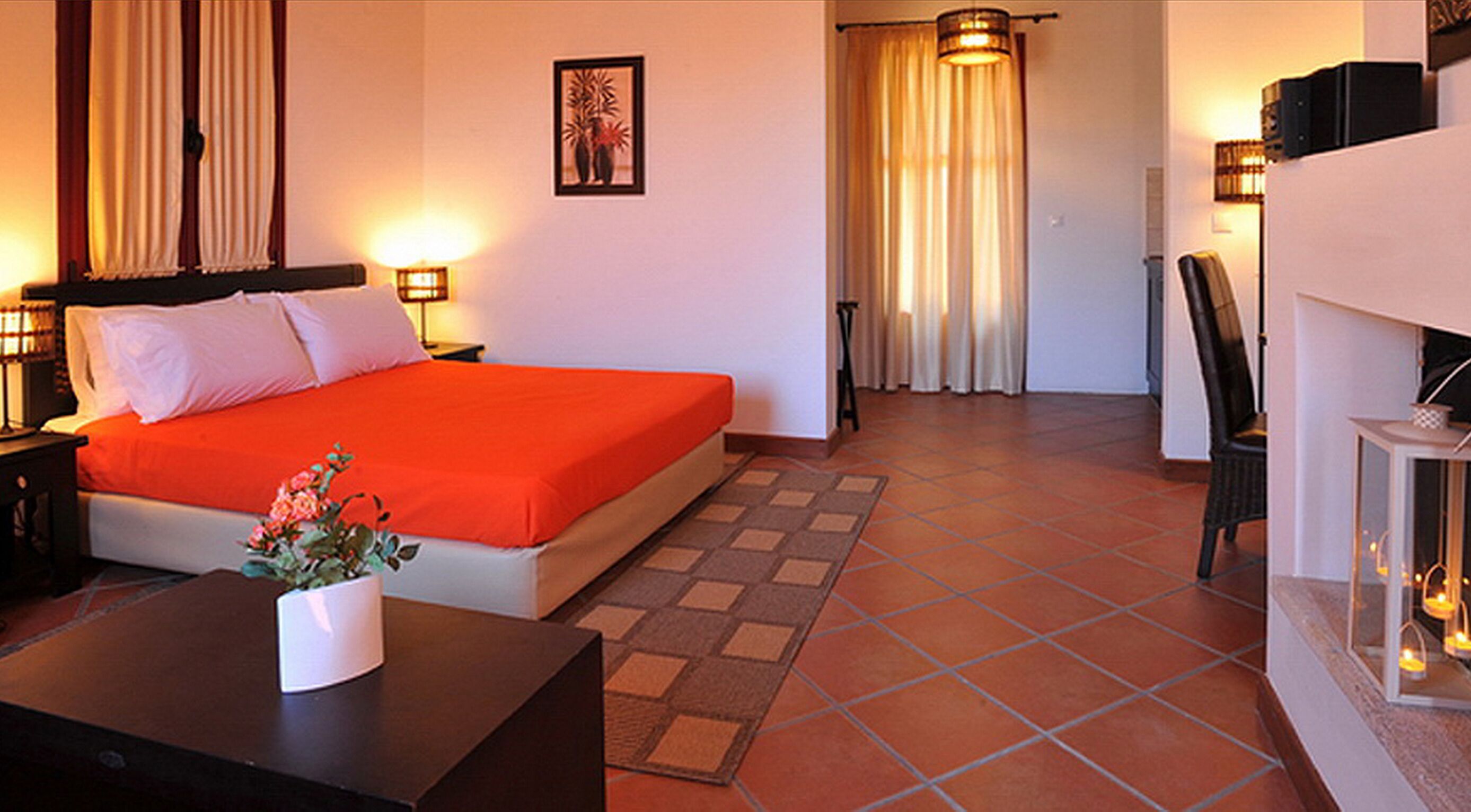 A hotel room with a bed, a nightstand, a desk, a chair, and a small table with a vase of flowers.