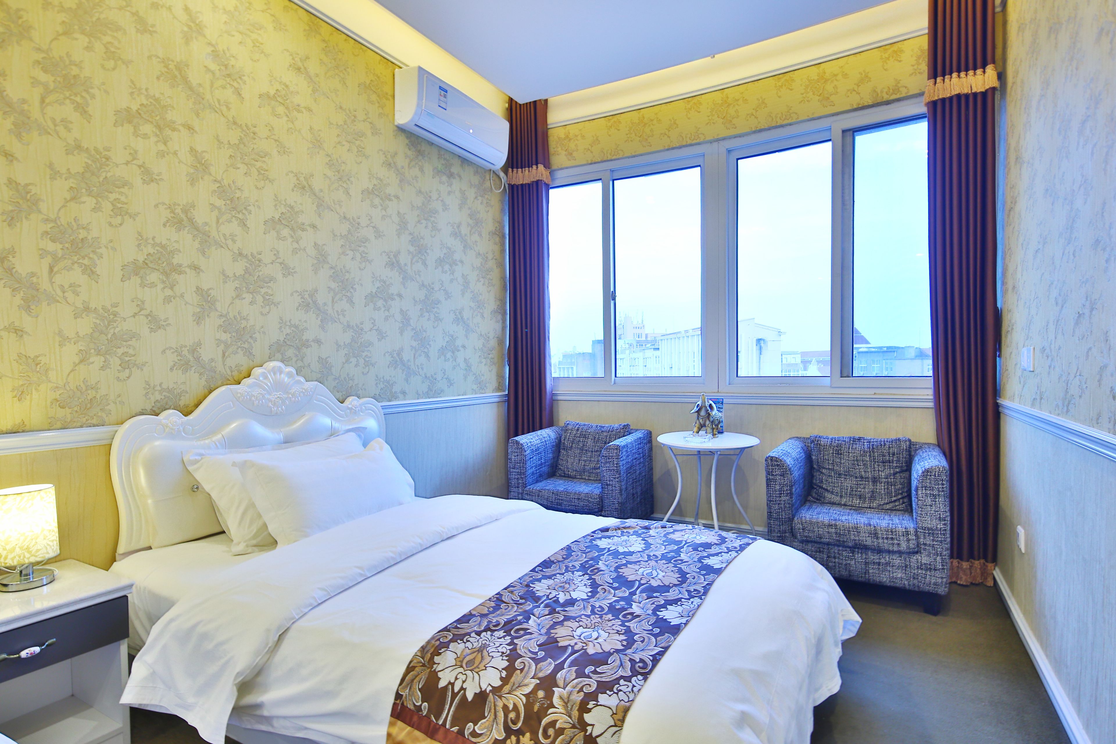 Una camera d'albergo con un letto grande, due poltrone, un tavolino e una finestra con tende.