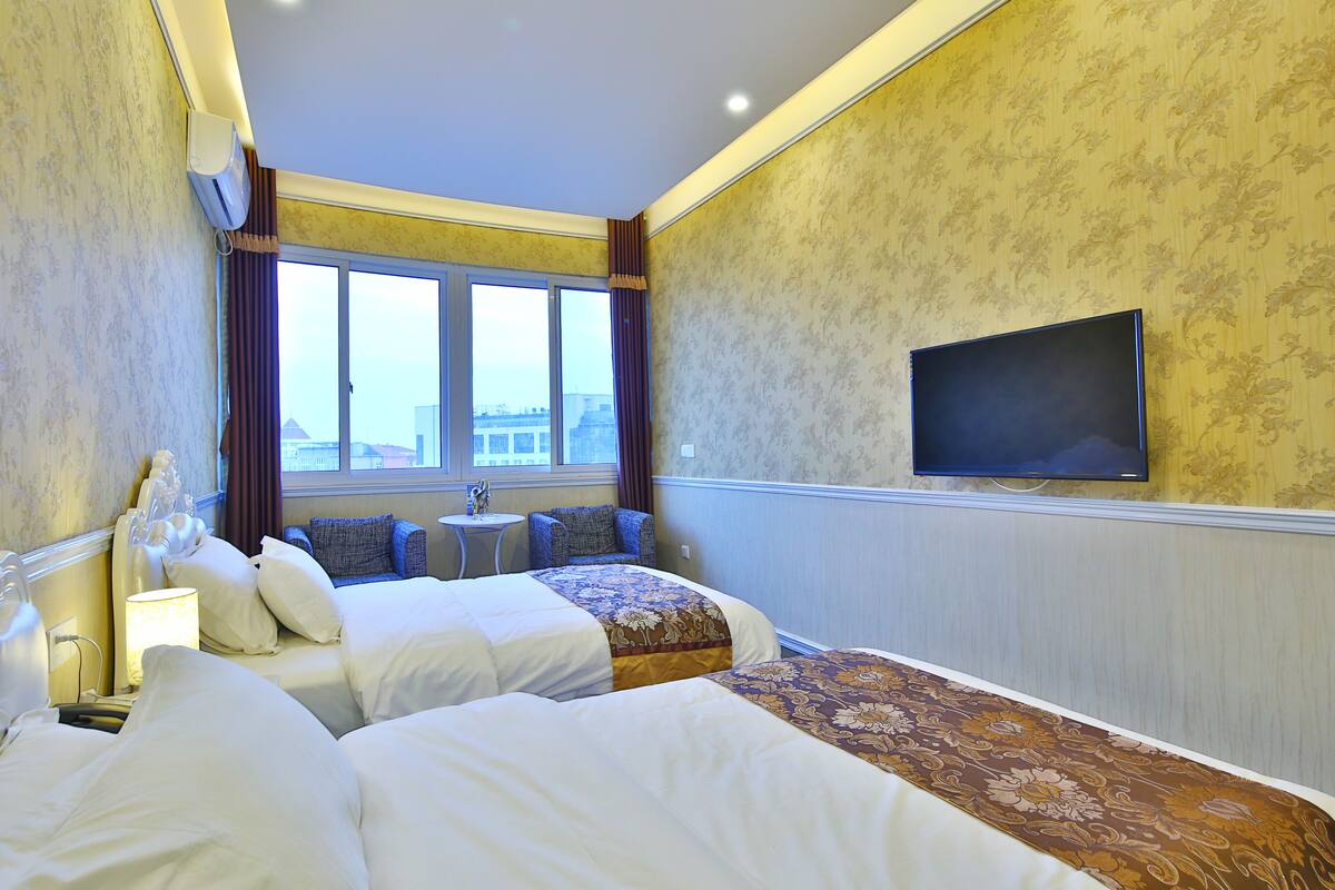 A hotel room with two beds, a television, a small table, and a window with curtains.