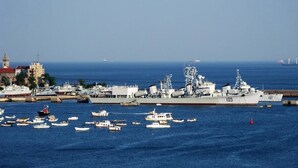 Un grand navire de guerre était amarré dans un port, avec de plus petits bateaux en premier plan.