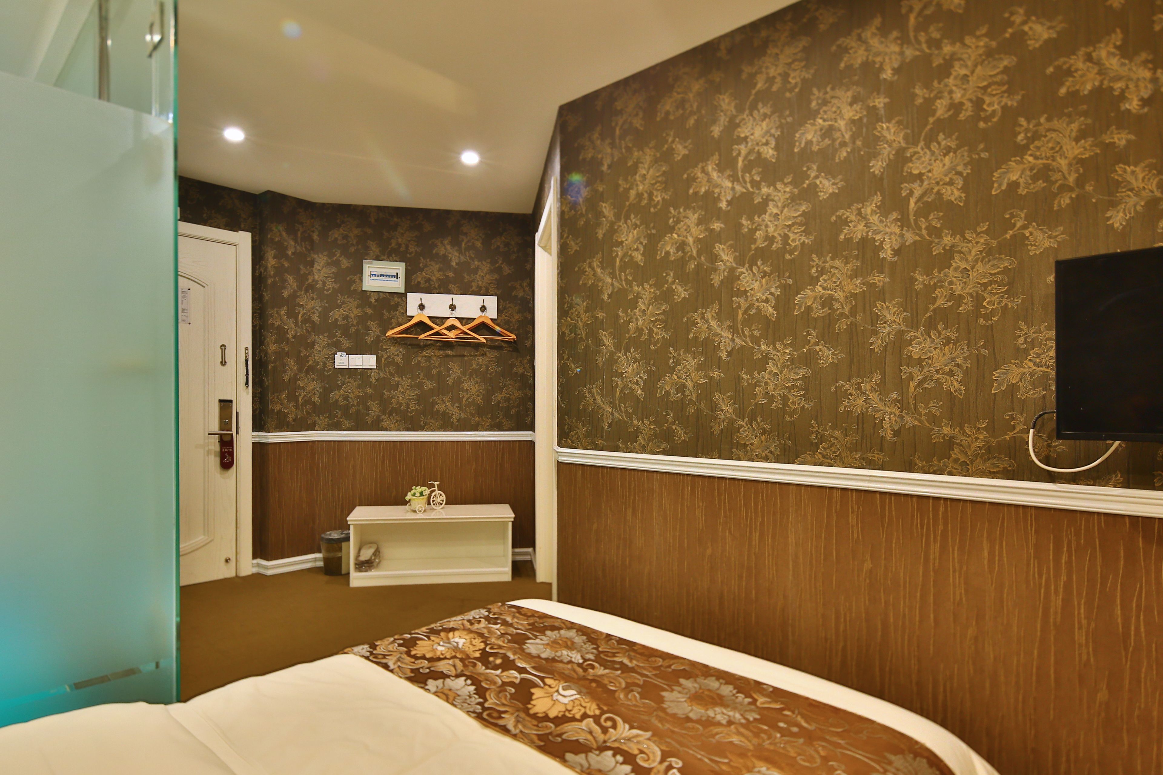 Una habitación de hotel con una cama, una mesita de noche pequeña, un televisor montado en la pared y una puerta que da a otra habitación.