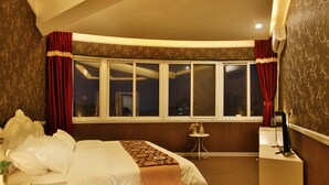 Une chambre d’hôtel avec un grand lit, une petite table, une chaise, un bureau et une fenêtre avec des rideaux.