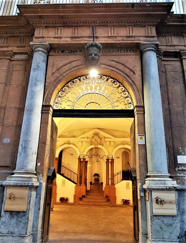 A grand entrance with a classical archway, a staircase leading inside, and a plaque with the name "VINC.NATOLI".