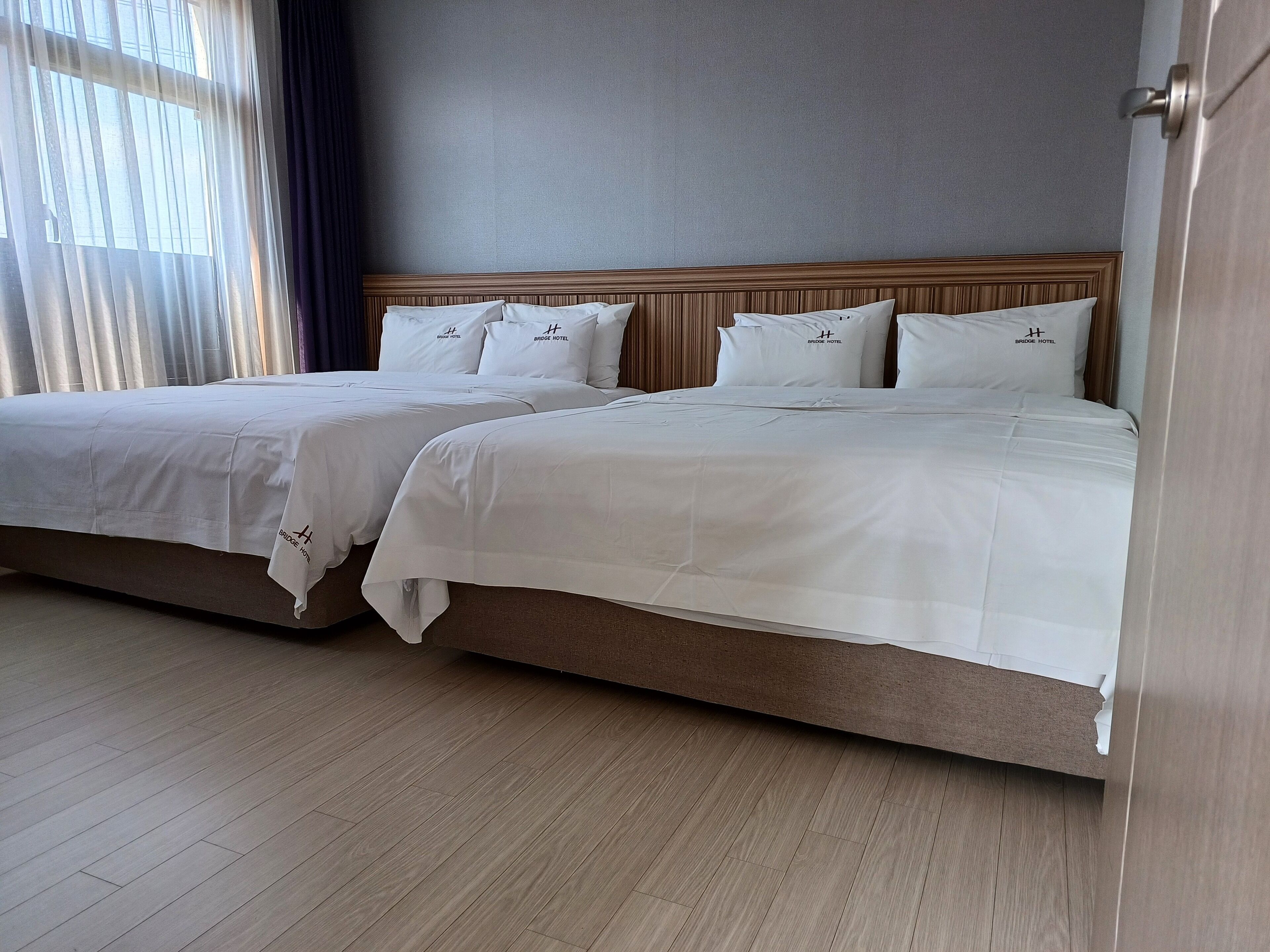 Habitació d'hotel amb dos llits, cadascun amb roba de llit i coixins blancs, un capçal de fusta i un sòl de fusta de color clar.