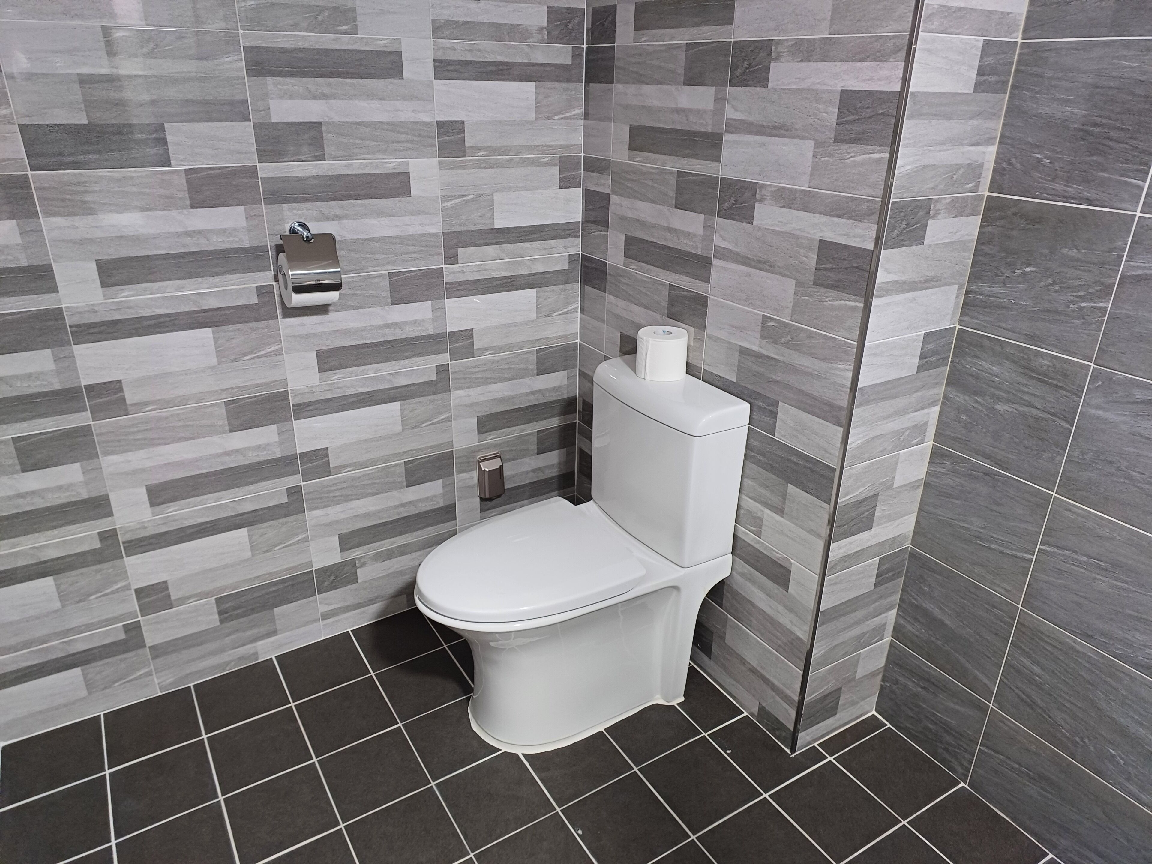 A modern bathroom with a toilet, a hand dryer, and a toilet paper holder on the wall.