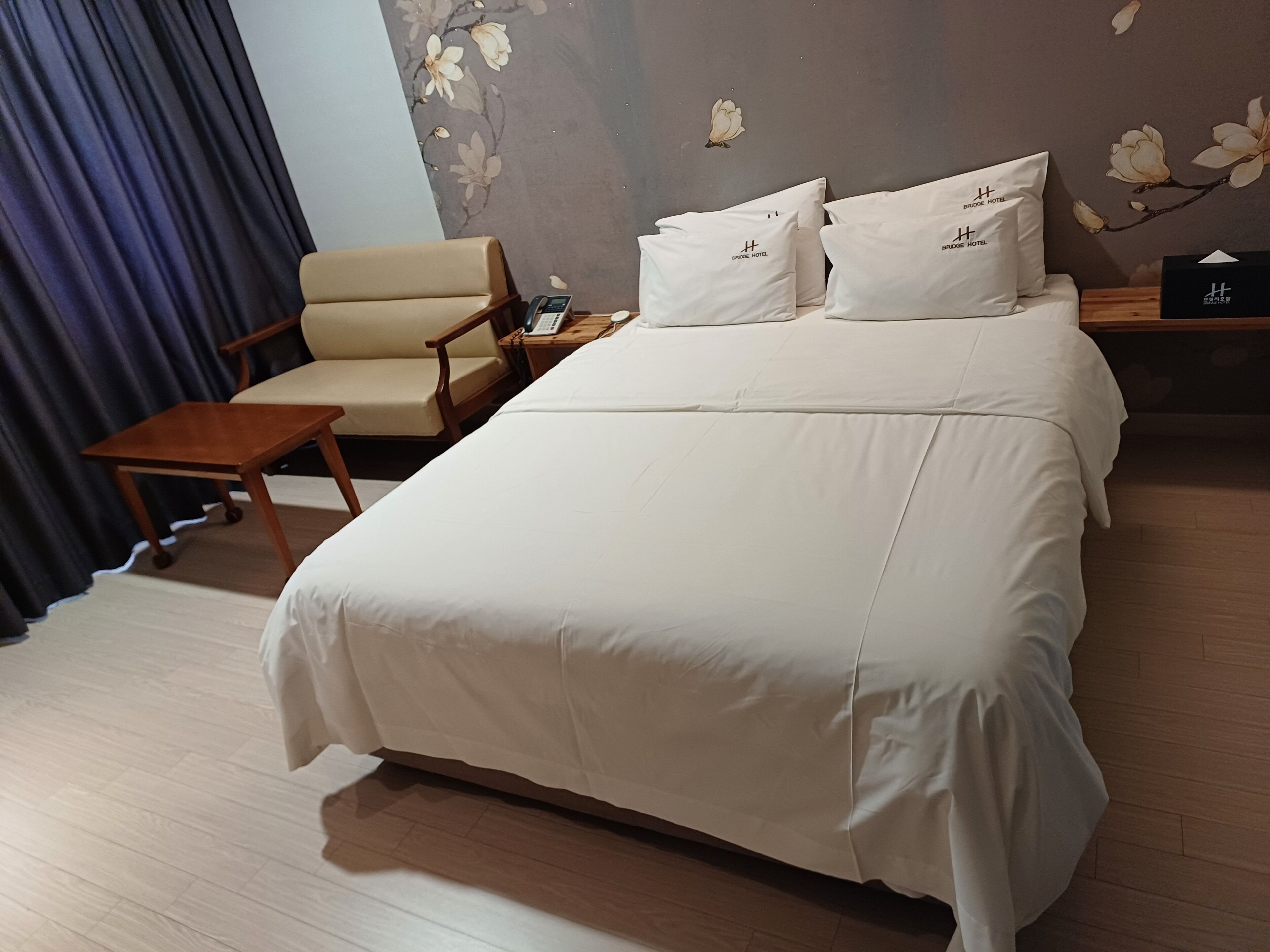 A hotel room with a bed, a chair, a small table, and a nightstand with a phone.