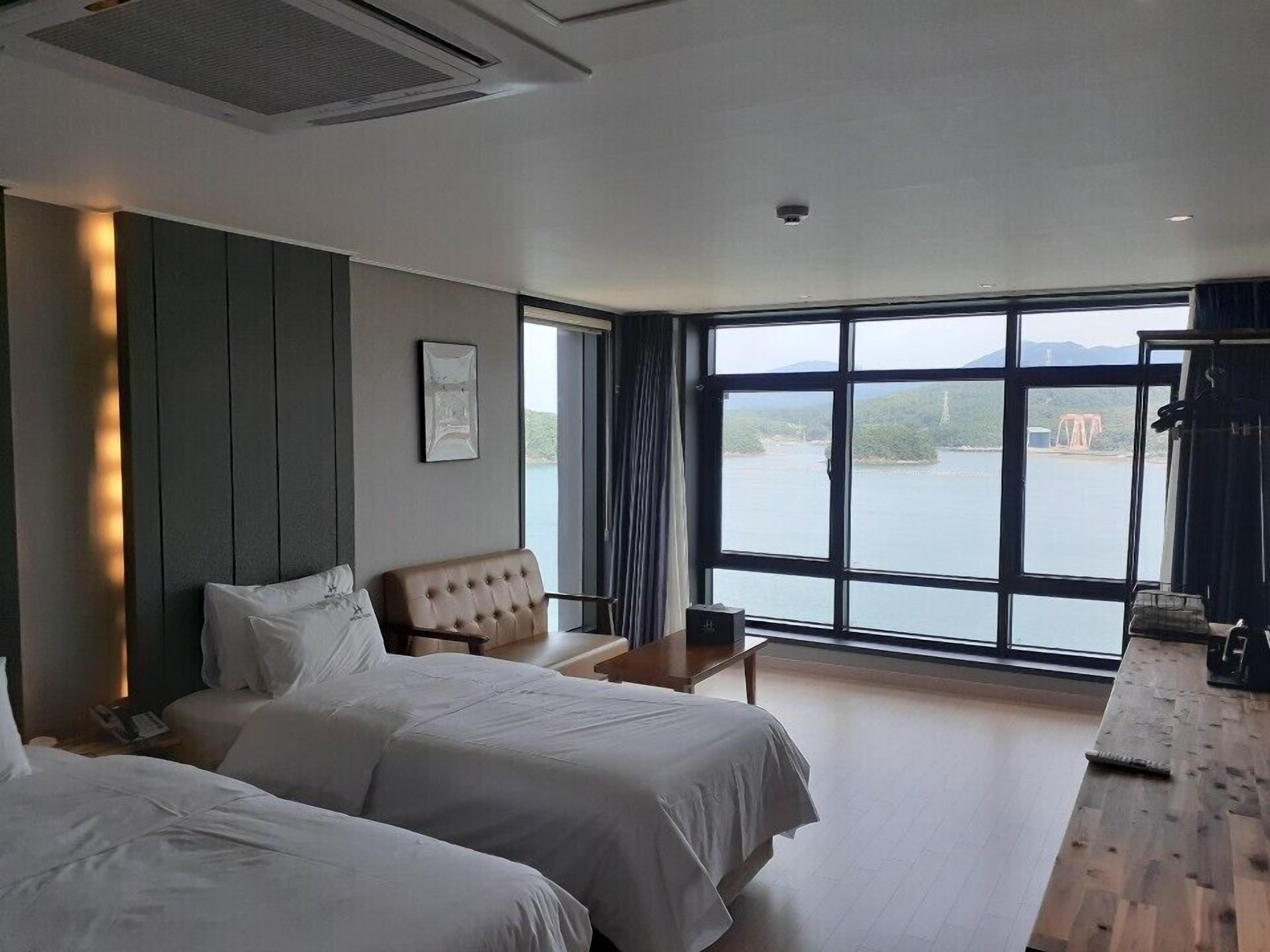 A hotel room with two beds, a large window with a view of a body of water, a desk, and a chair.