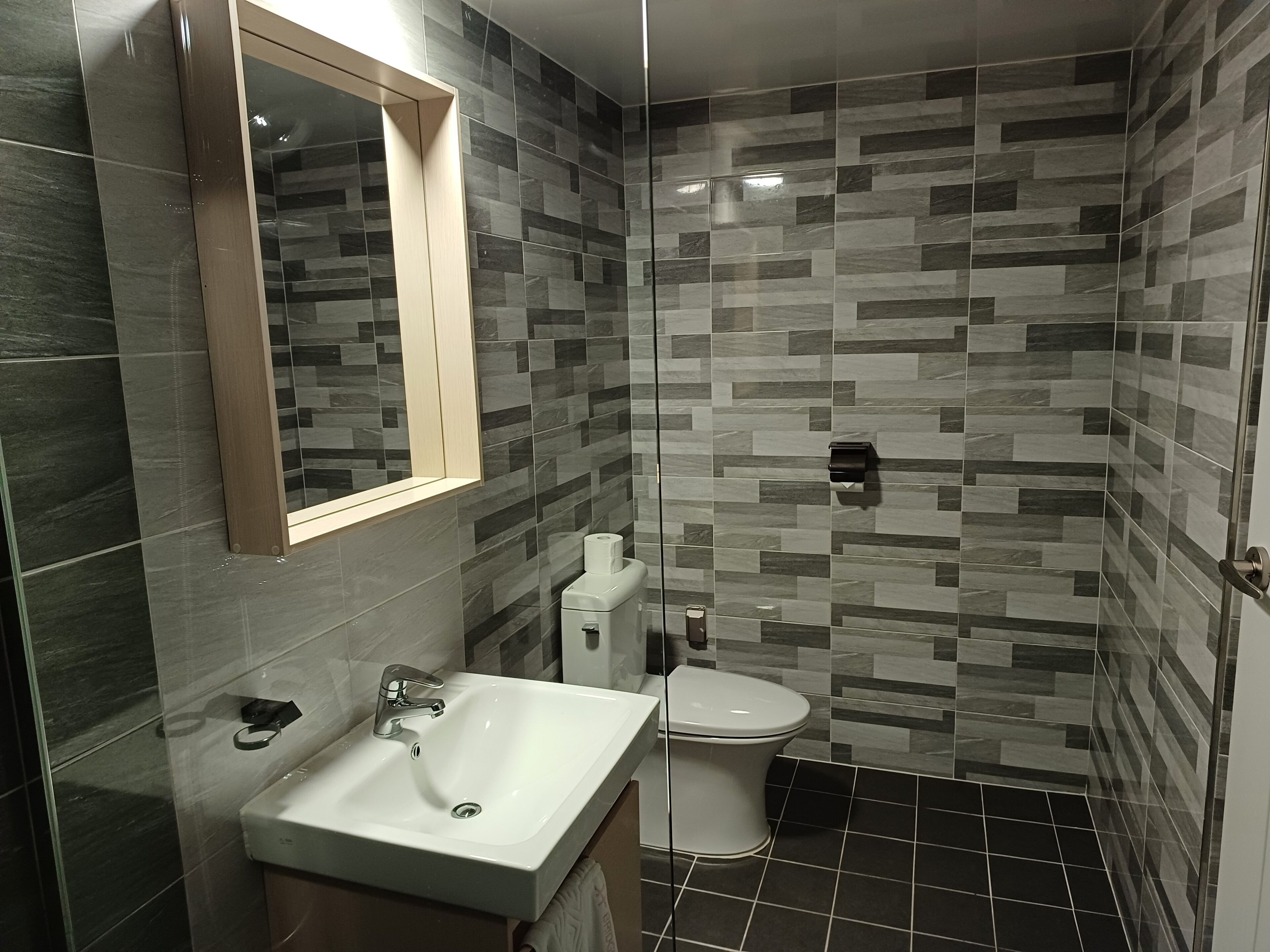 Un bany modern amb boxa de dutxa de vidre, un lavabo blanc i un vàter.