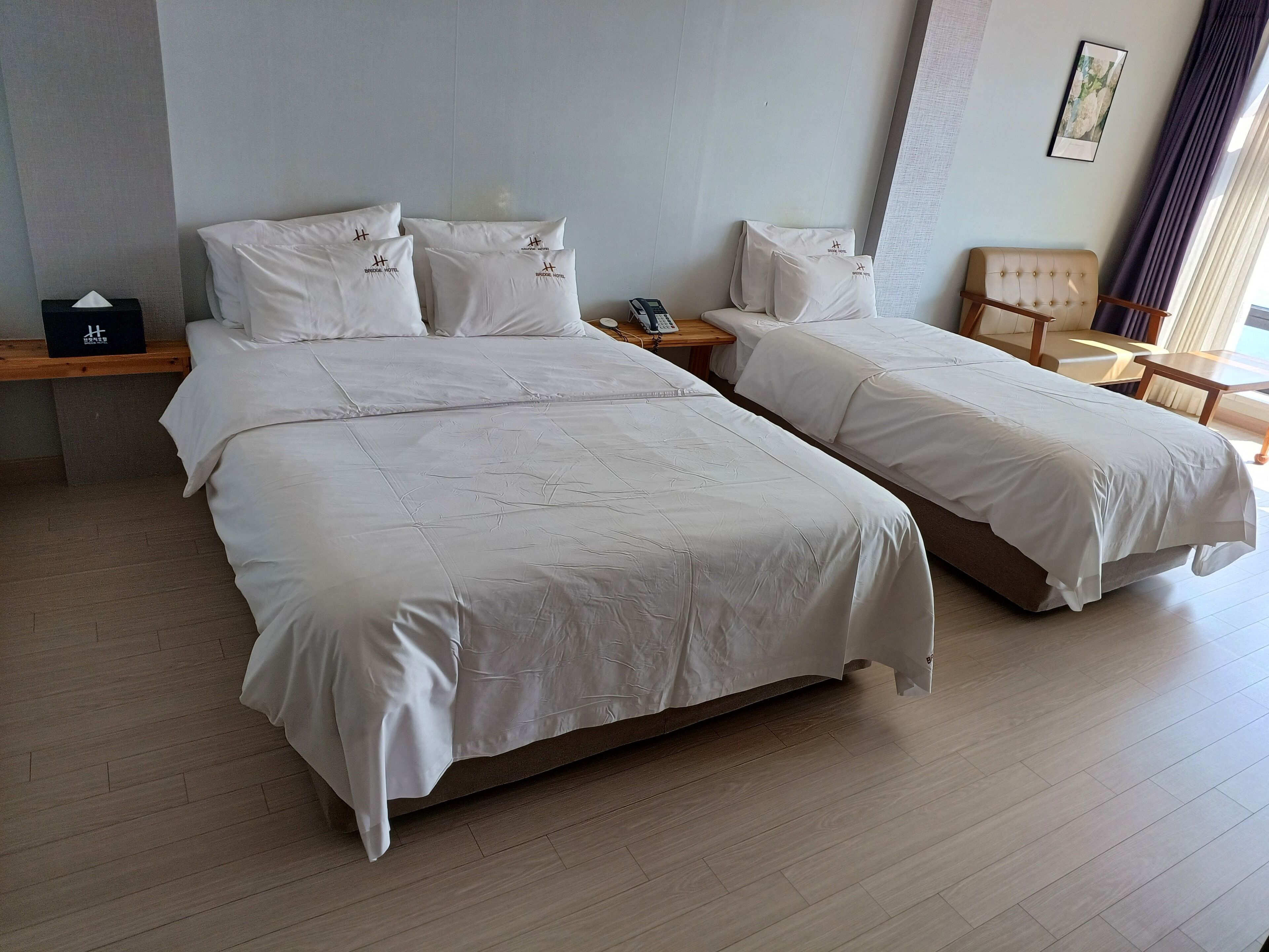A hotel room with two beds, a nightstand, a chair, and a small table.