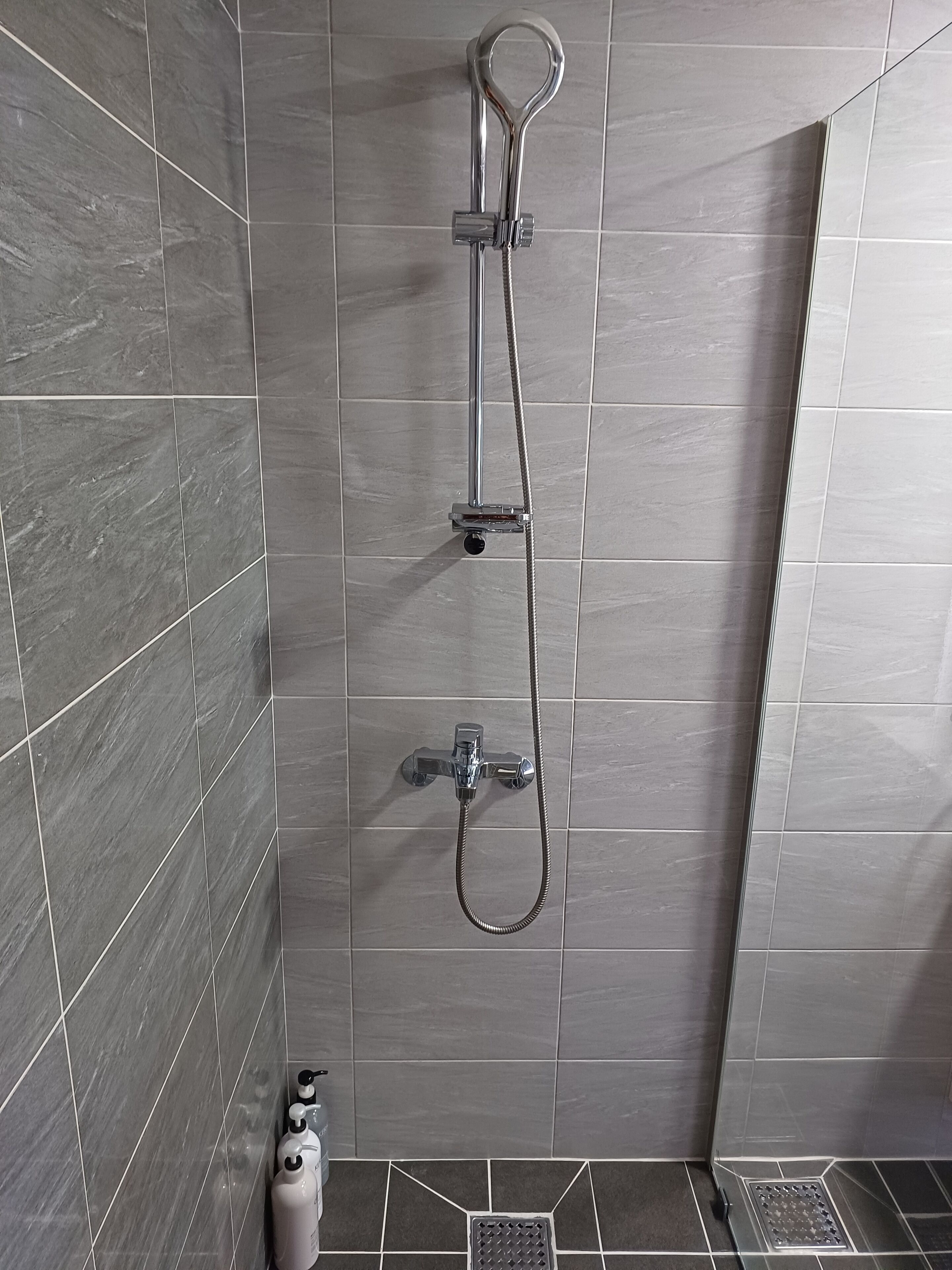 Ducha con cabezal de ducha de mano y grifo empotrado, paredes con azulejos y desagüe.