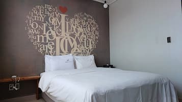 A bedroom with a bed, pillows, a nightstand, and a wall with a heart-shaped word cloud design.