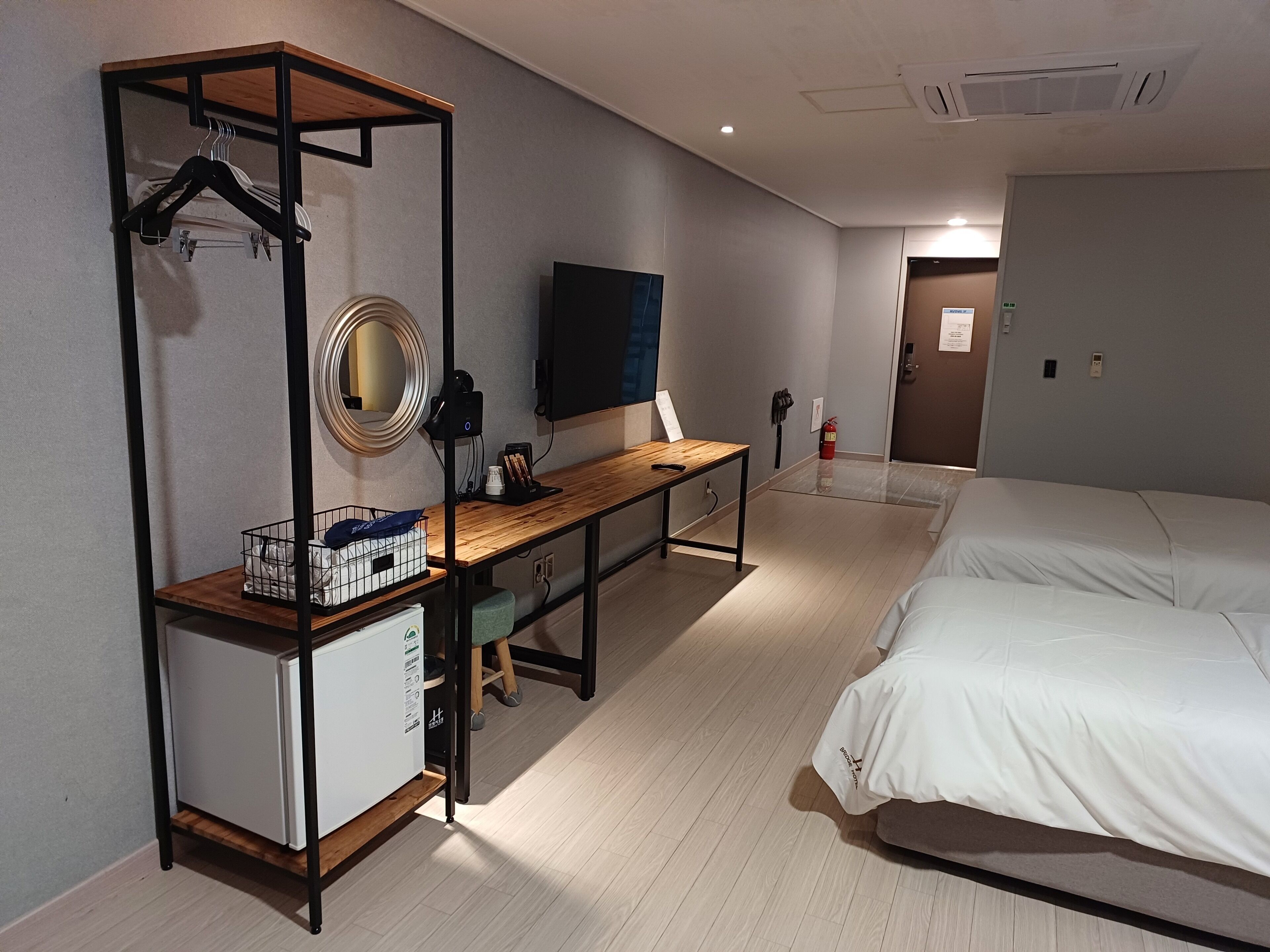 A hotel room with a bed, a desk with a mirror, a television, and a small refrigerator.