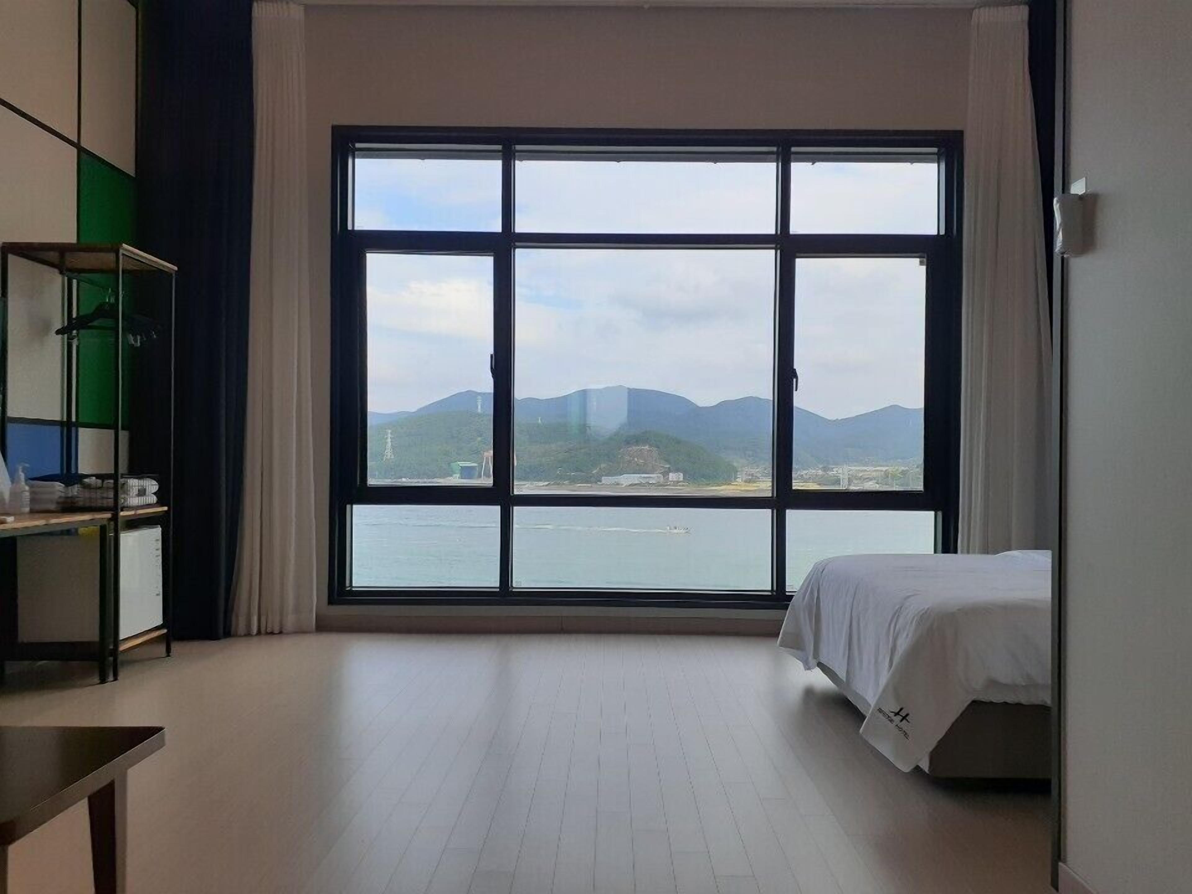 Quarto de hotel com uma janela grande, uma cama, uma escrivaninha e uma cadeira.