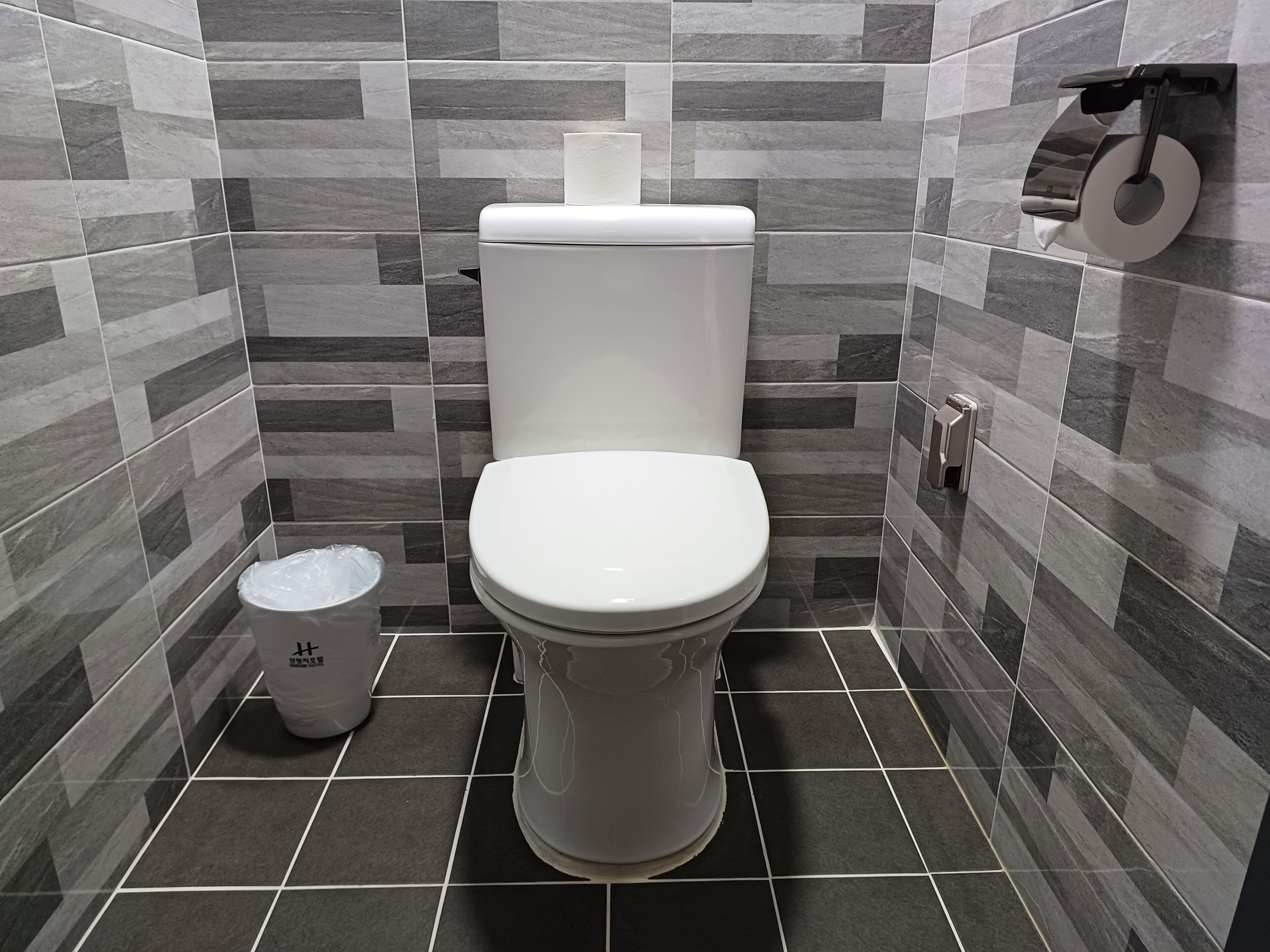 A bathroom with a toilet, a trash bin, and a toilet paper holder on the wall.