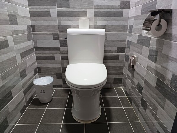 Un baño con un inodoro, un cubo de basura y un dispensador de papel higiénico en la pared.