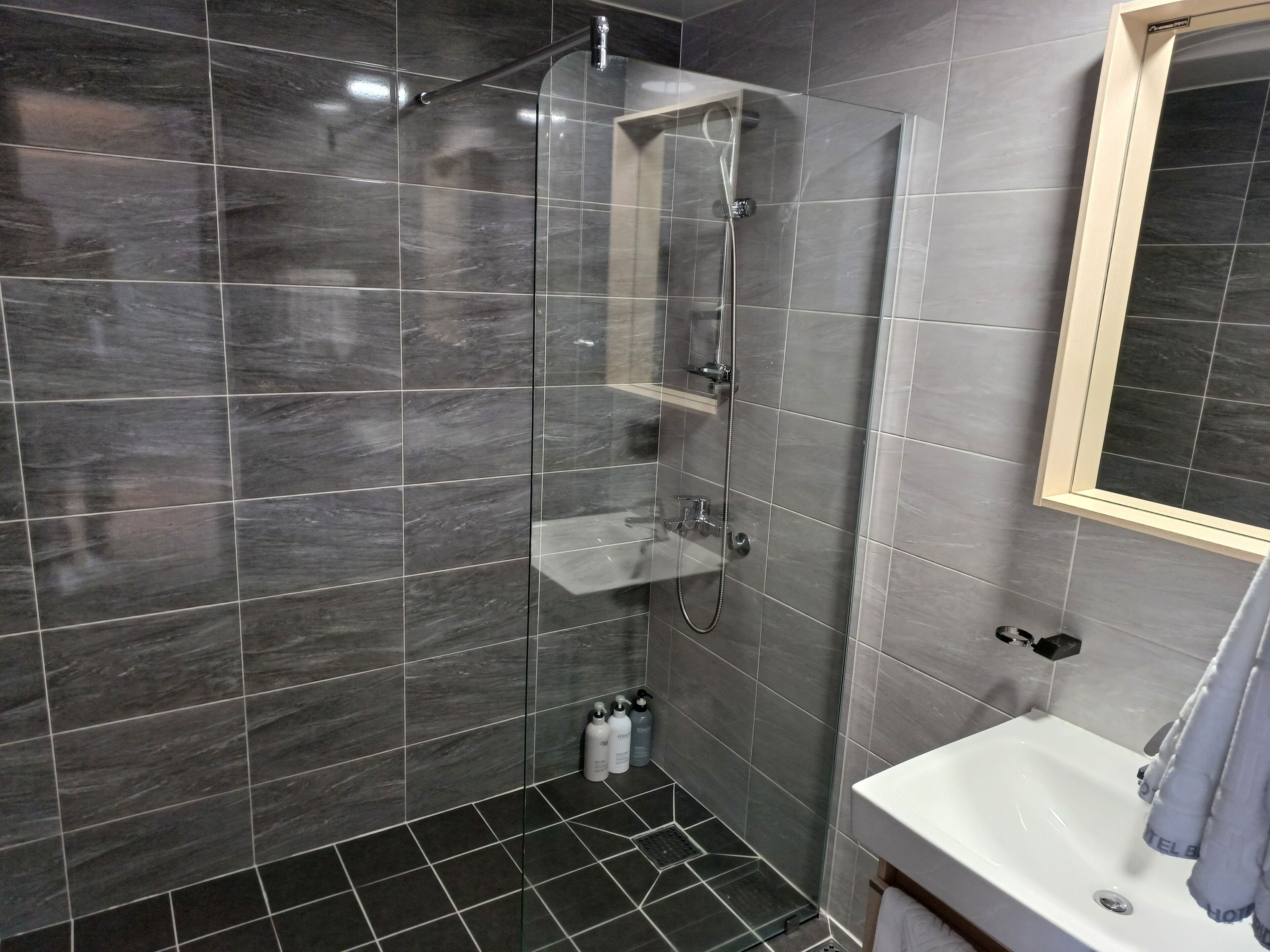A modern bathroom with a glass-enclosed shower, a white sink, and a mirror above it.
