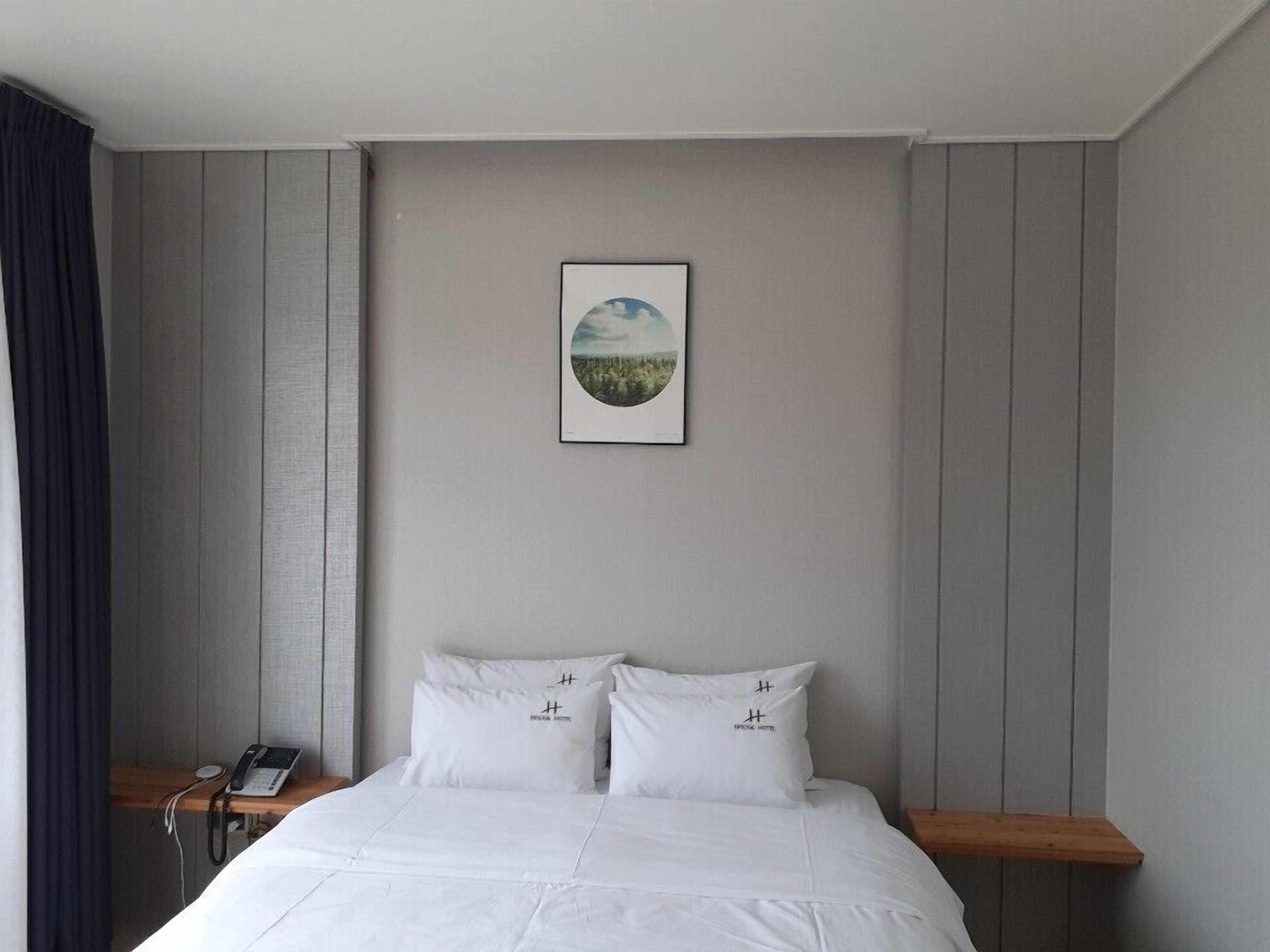 Una habitación de hotel con una cama, una mesita de noche con un teléfono y un cuadro en la pared.
