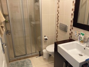 Een badkamer met een douchecabine van glas, een toilet, een wastafel en een spiegel.