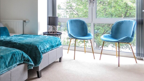 A bedroom with a bed, two chairs, a lamp, and a large window with a view of trees.