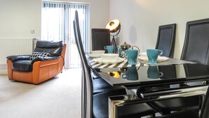 A room with a dining table set for four, a black leather chair, a standing lamp, and a radiator.