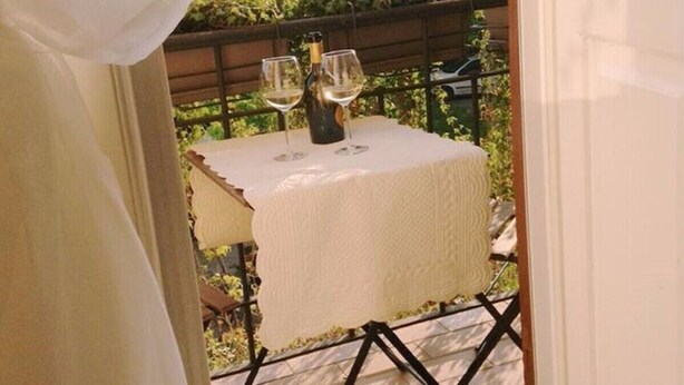 Une table avec une bouteille et des verres sur un balcon donnant sur un paysage verdoyant.