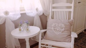 Une chaise blanche avec un coussin en forme de cœur, une petite table ronde ornée de vases et de fines rideaux blancs.
