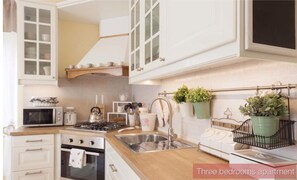 Appartamento con tre camere da letto e cucina dotata di mobili bianchi, forno a microonde, fornello e lavello.