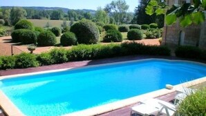 Ein rechteckiger Swimmingpool mit umlaufender Holzterrasse, eingebettet in einen angelegten Garten mit ordentlich geschnittenen Sträuchern und Bäumen.