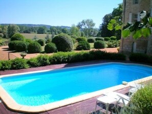 Ein rechteckiger Swimmingpool mit umlaufender Holzterrasse, eingebettet in einen angelegten Garten mit ordentlich geschnittenen Sträuchern und Bäumen.