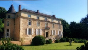 Ein großes Steinhaus mit einem zentralen Turm, zahlreichen Fenstern und einem gepflegten Garten.