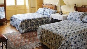Ein Zimmer mit zwei Betten, einer Kandelaber, einem Tisch mit Lampe und einem Fenster mit Vorhängen.