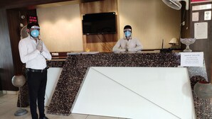 A reception desk with two staff members wearing masks, a digital clock, and a sign indicating check-out times. - Hotel Maple Delite (Lucknow)