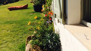 Ein Haus mit Garten, einer großen Pflanze im Topf und einem Boot im Hintergrund.