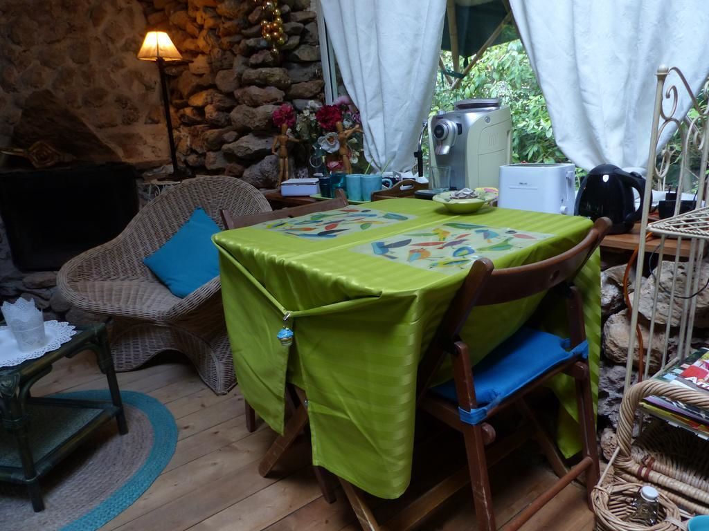 Una habitación acogedora con una mesa de madera cubierta por un mantel verde, sillas de mimbre, una pared de piedra y una ventana con cortinas.