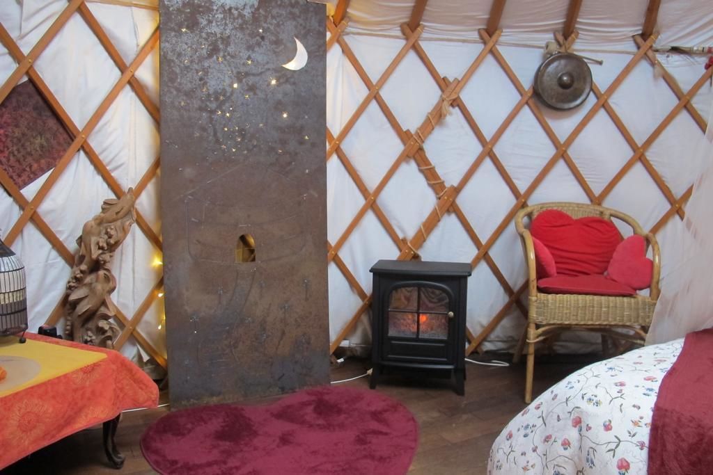 Una habitación acogedora con un muro de celosía de madera, una estufa pequeña, una silla de mimbre con cojín rojo y una mesa con mantel rojo.