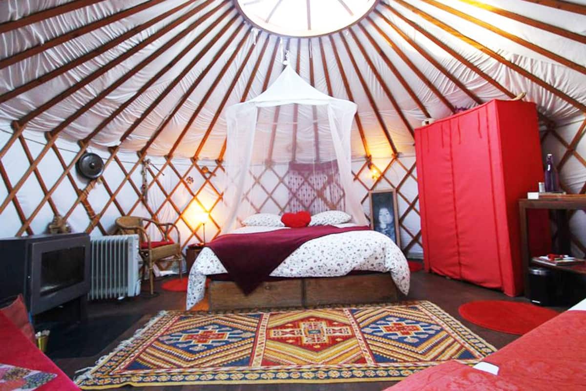 L’intérieur d’une yourte, avec un lit, une armoire rouge et un tapis à motifs.