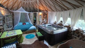 Een gezellig interieur van een joert met een bed, een jacuzzi en een klein zithoekje.