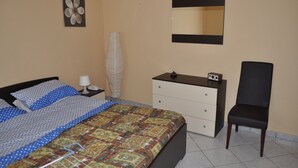 A bedroom with a bed, a dresser, a chair, a mirror, and a vase on the wall.