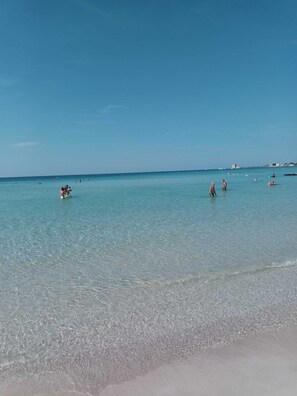 Una platja amb aigua cristal·lina i gent nedant.