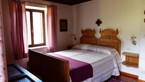 Une chambre à coucher avec un lit en bois, une petite table de chevet, une fenêtre avec des rideaux et un luminaire fixé au mur.