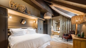 A bedroom with a large bed, wooden beams, a hanging light fixture, and a view of a dining area.