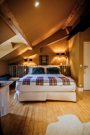 Een knus slaapkamer met een groot bed, houten balken, een schuin dak en een klein bureau met stoel.