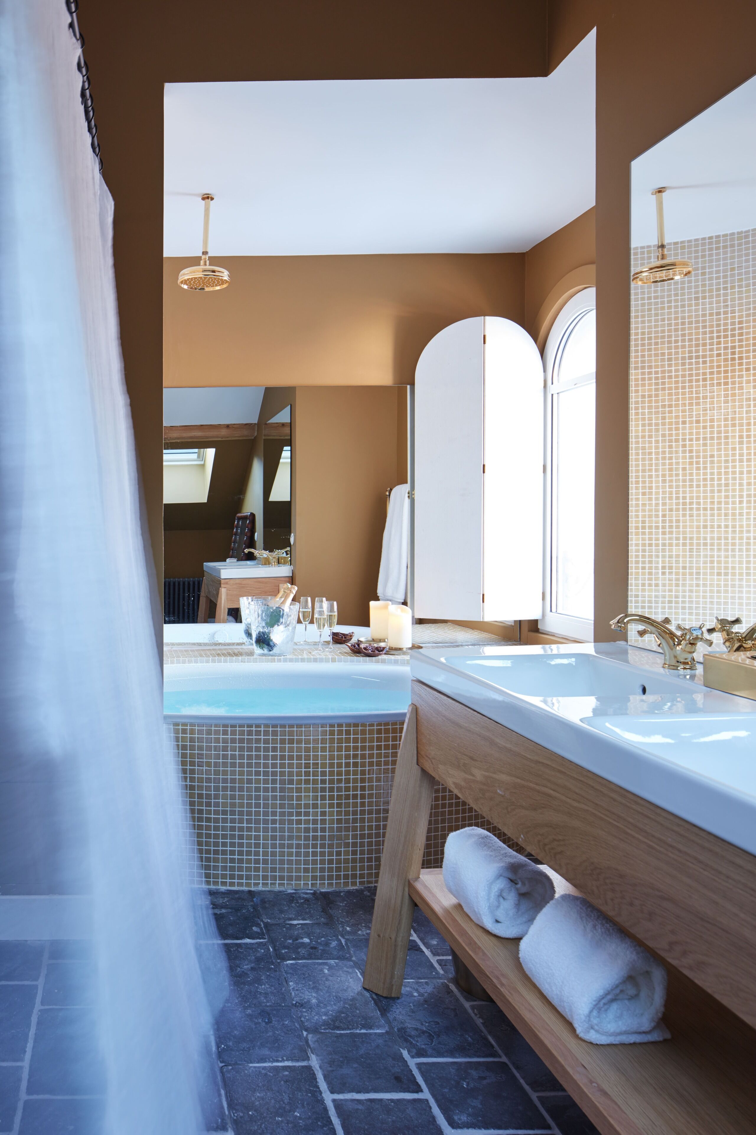 A modern bathroom with a large bathtub, a wooden bench with towels, and a large mirror.