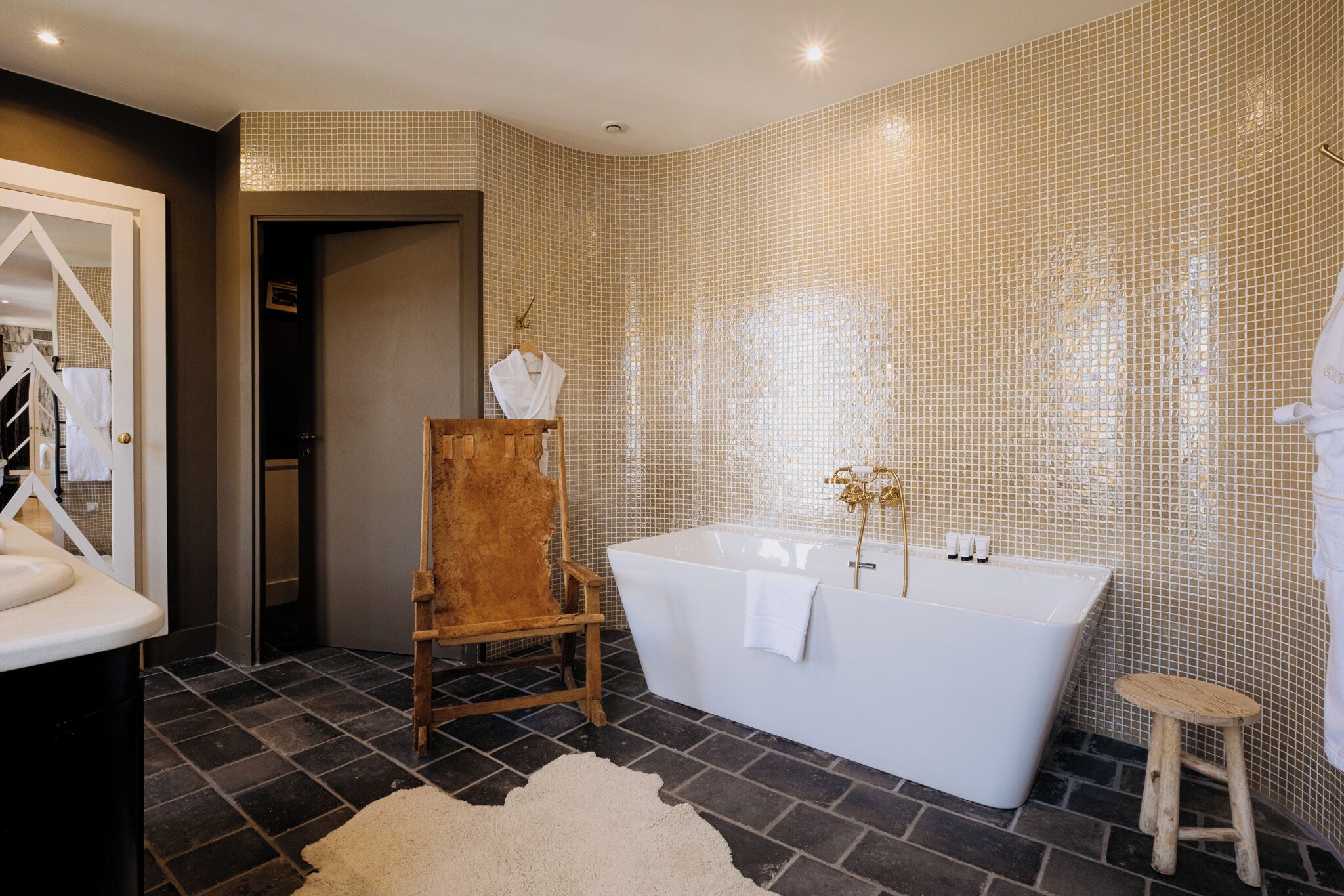 A modern bathroom with a freestanding bathtub, a wooden chair, and a small stool.
