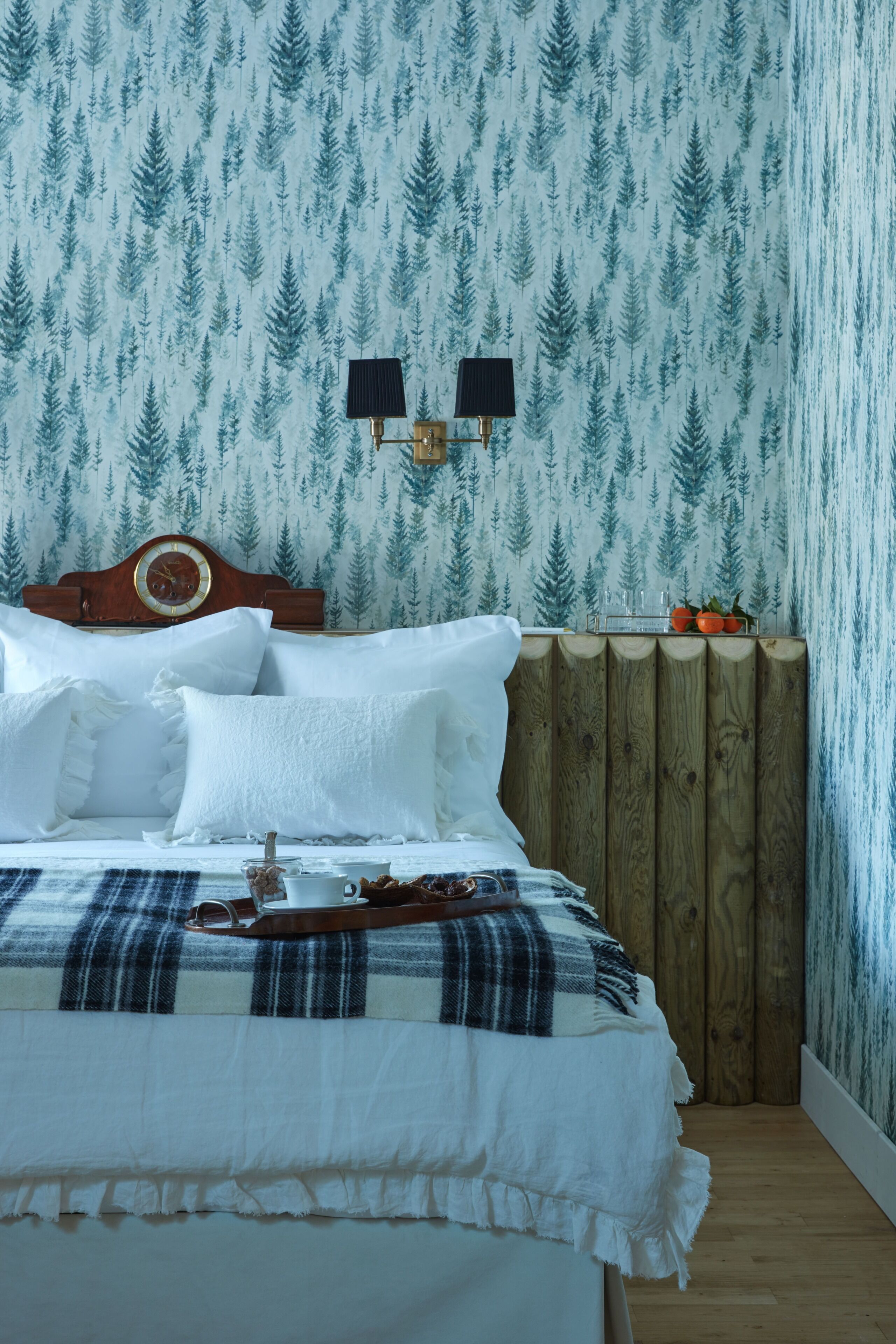 Un dormitorio con cama, cabecero de madera, mesita de noche y pared con estampado de bosque.