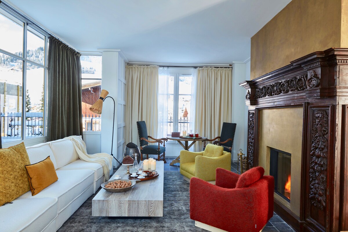 A modern living room with a white sofa, red and yellow chairs, a coffee table with snacks, and a fireplace.