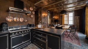 A modern kitchen with a large island, stainless steel appliances, copper cookware, and a rustic wooden ceiling.